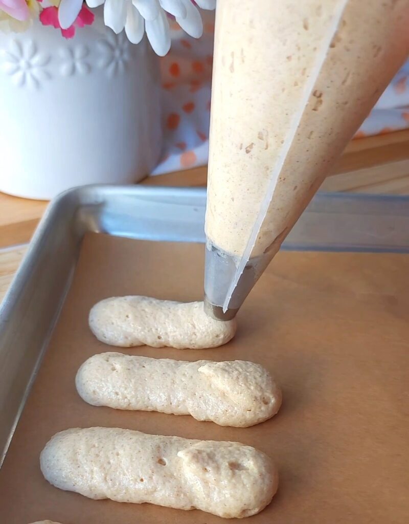 Piping homemade ladyfingers onto parchment paper