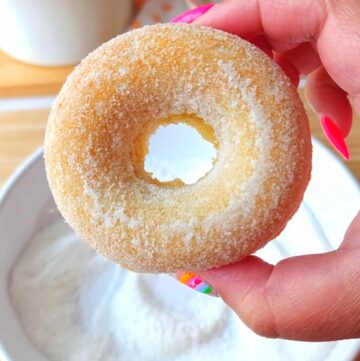 Sugar free baked donut hovering over a bowl of monk fruit sweetener