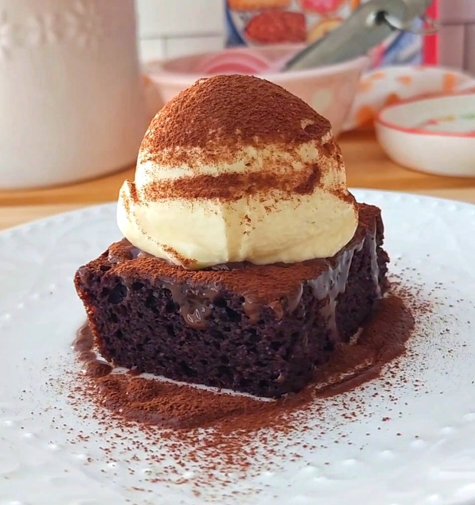 Slice of chocolate cake topped with ganache and mascarpone cream on a white plated. Dusted with cocoa powder