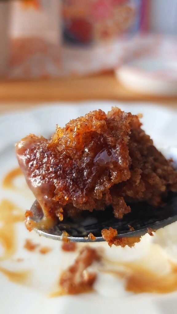 Up close photo of a bite of extra gooey pudding glistening with sweet toffee sauce